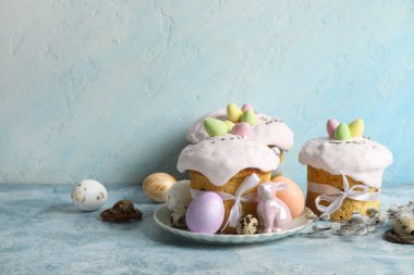 Lezzetli dekore edilmiş Paskalya pastaları, porselen tavşanlar ve renkli arka planda tabakta boyanmış yumurtalar.