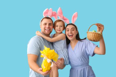 Mavi arka planda Paskalya dekoru olan tavşan kulaklı mutlu bir aile.