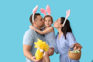 Mavi arka planda Paskalya dekoru olan tavşan kulaklı mutlu bir aile.