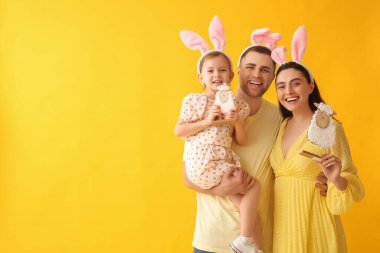 Paskalya tavşanı kulaklı mutlu bir aile. Sarı arka planda oyuncak koyunları var.