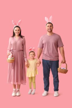 Tavşan kulaklı mutlu aile pembe arka planda paskalya yumurtası dolu sepetler tutuyor.