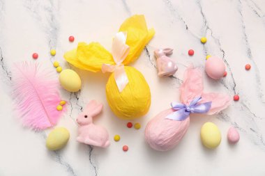Kağıda sarılmış boyanmış Paskalya yumurtaları ve beyaz grunge arka planda tavşanlar.