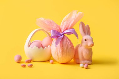 Oyuncak tavşanlı seramik sepet ve sarı arka planda Paskalya yumurtaları.