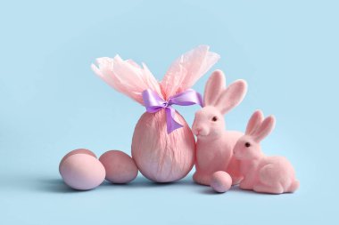 Kağıda sarılmış boyanmış Paskalya yumurtaları ve mavi arka planda oyuncak tavşancıklar.