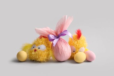 Kağıda sarılmış boyanmış Paskalya yumurtaları ve gri arka planda piliç oyuncakları.