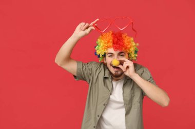 Kırmızı arka planda komik kılık değiştirmiş yakışıklı bir genç. 1 Nisan kutlamaları