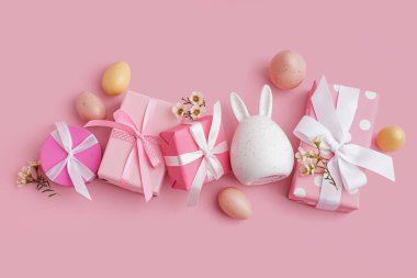 Hediye kutularıyla boyanmış Paskalya yumurtaları ve pembe arka planda bir tavşan.