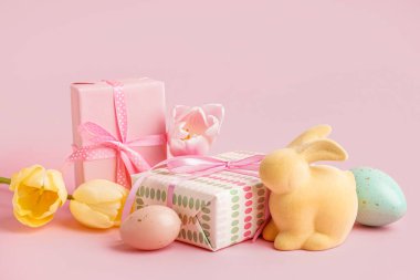 Lale çiçekli hediye kutuları ve pembe arka planda Paskalya oyuncak tavşanı.