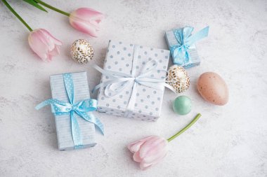 Hediye kutularıyla boyanmış Paskalya yumurtaları ve beyaz grunge arka planda lale çiçekleri.