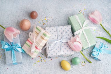 Hediye kutularıyla boyanmış Paskalya yumurtaları ve beyaz grunge arka planda lale çiçekleri.