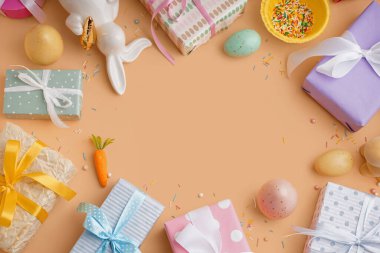 Hediye kutuları ve turuncu arka planda tavşanla boyanmış Paskalya yumurtalarından yapılmış çerçeve.