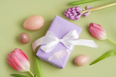 Hediye kutusuyla boyanmış Paskalya yumurtaları ve yeşil arka planda çiçekler.