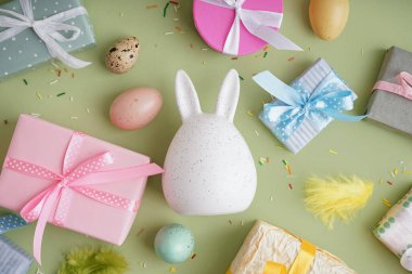 Hediye kutularıyla boyanmış Paskalya yumurtaları ve yeşil arka planda bir tavşan.