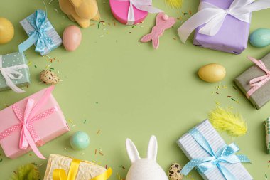 Yeşil arka planda hediye kutuları ve tavşanlarla boyanmış Paskalya yumurtalarından yapılmış çerçeve.