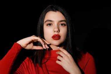Siyah arka planda kırmızı dudakları olan güzel genç bir kadın.