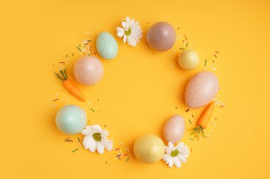 Paskalya yumurtalarından, kasımpatı çiçeklerinden ve turuncu arka planda havuçlardan yapılmış güzel bir çelenk.