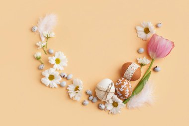 Çiçekli kompozisyon, bej arka planda Paskalya yumurtası ve tüyleri