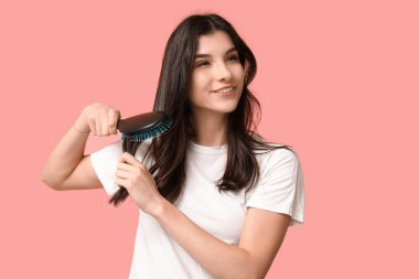 Güzel genç bir kadın pembe arka planda saçını tarıyor.