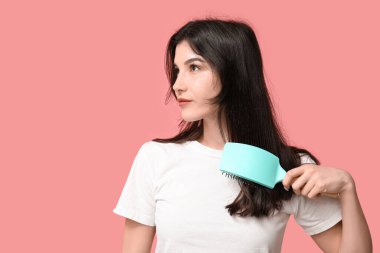 Güzel genç bir kadın pembe arka planda saçını tarıyor.