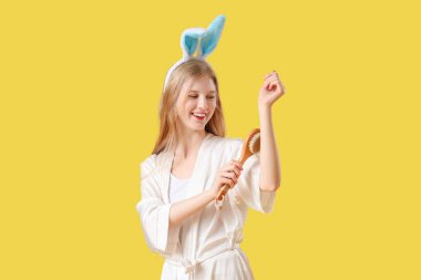 Sarı arka planda masaj fırçası olan tavşan kulaklı güzel bir kadın.