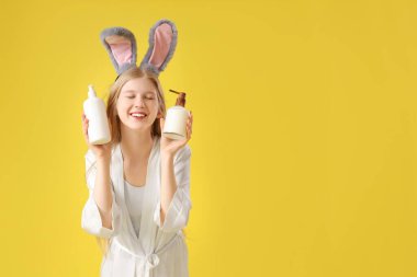 Tavşan kulaklı güzel bir kadın sarı arka planda kozmetik ürünler taşıyor.