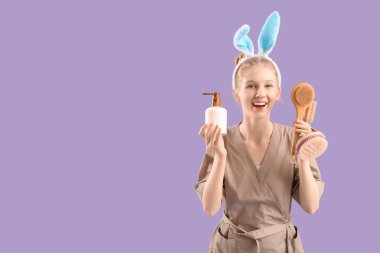 Tavşan kulaklı duygusal kadın masaj terapisti elinde fırça ve renkli arka planda bir şişe kozmetik ürünü tutuyor.