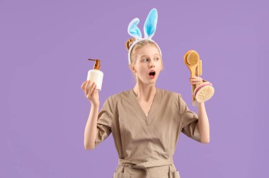 Tavşan kulaklı duygusal kadın masaj terapisti elinde fırça ve renkli arka planda bir şişe kozmetik ürünü tutuyor.