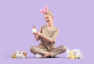 Mutlu kadın masaj terapisti Paskalya dekorasyonu ve spa malzemeleri ile renkli arka planda oturuyor.