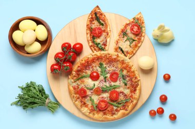 Tavşan kulaklı Paskalya pizzası, mavi arka planda yumurta ve domates.