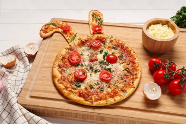 Lezzetli Paskalya pizzası, tavşan kulaklı, peynirli ve domatesli beyaz ahşap arka planda.