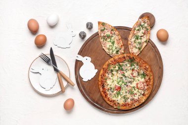 Paskalya pizzası, tavşan kulağı, çatal bıçak takımı ve beyaz arka planda yumurta.