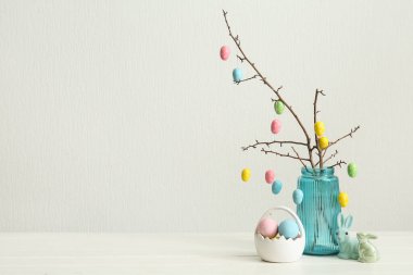 Mavi cam vazoda Paskalya yumurtaları ve beyaz arka planda Paskalya dekoru olan dallar.