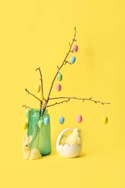 Mavi cam vazoda Paskalya yumurtaları, sarı arka planda tavuklar ve tavuklar.