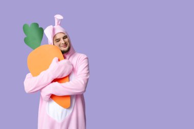 Leylak kaplamalı kağıt havuçlu tavşan kostümlü genç adam. Paskalya kutlaması