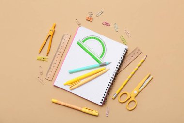 Bej arka planda açıölçer ve kalemlerle dolu bir defter. Üst görünüm