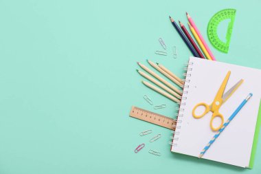 Turkuaz arka planda defter, kalem ve makas. Üst görünüm