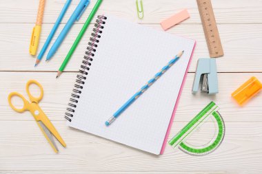 Beyaz ahşap zemin üzerinde makas ve zımba bulunan defter. Üst görünüm