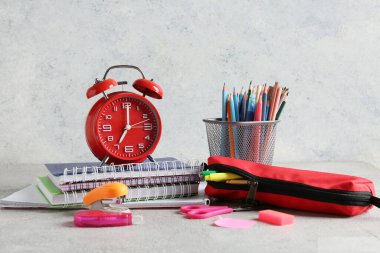 Alarm saati, kalem kutusu ve defterler gri arkaplana karşı masada