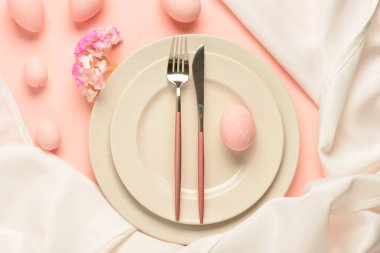 Paskalya yumurtaları, peçete ve pembe arka planda çiçeklerle dolu şirin bir masa.