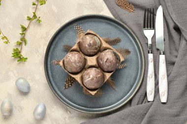 Boyanmış Paskalya yumurtaları, dalları ve gri grunge arka planda peçetesi olan şenlik masası.