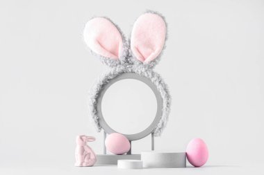Tavşan kulaklı dekoratif podyumlar, paskalya yumurtaları ve gri arka planda oyuncak tavşan.