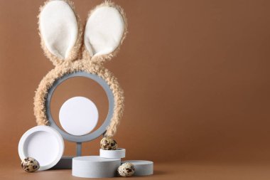 Paskalya yumurtaları ve kahverengi arka planda tavşan kulakları olan dekoratif podyumlar.