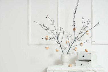 Ağaç dalları olan vazolar, Paskalya yumurtaları ve çekmeceler ışık duvarının yanındaki masada.