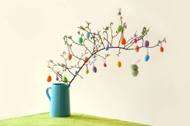 Ağaç dalları ve renkli Paskalya yumurtaları olan vazo ışıklı duvarın yanında.