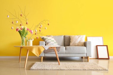 Ağaç dalları olan vazolar, oturma odasındaki masada Paskalya yumurtaları ve laleler.