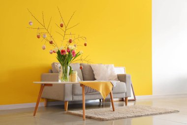 Ağaç dalları olan vazolar, oturma odasındaki masada Paskalya yumurtaları ve laleler.