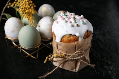 Tatlı Paskalya pastası, mimoza çiçekleri ve siyah arka planda yumurtaları olan tutucu.