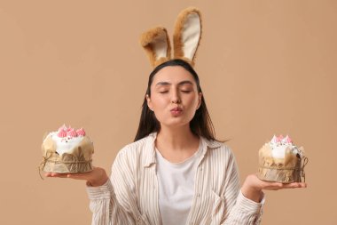 Kahverengi arka planda Paskalya pastaları olan tavşan kulaklı güzel bir genç kadın.