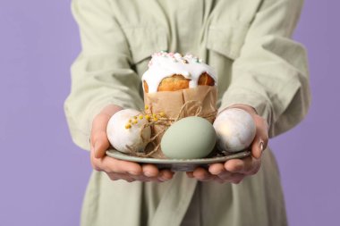 Paskalya pastası ve leylak arkaplanda yumurtaları olan genç bir kadın.