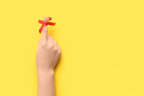 Female hand with red bow on index finger against yellow background. Reminder concept